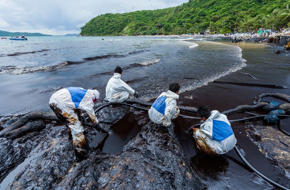four men in safety suits working on a shore to clean up oil spill