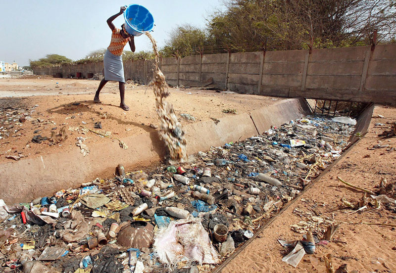 a woman dumping a pail of garbage into a water canal full of trashes